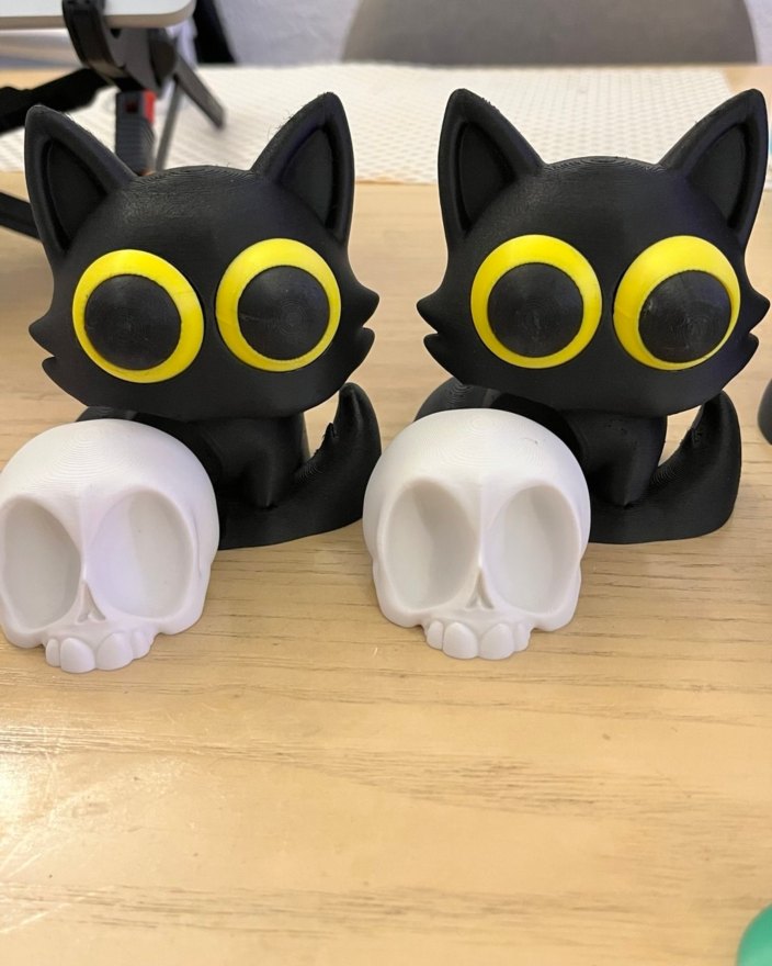 Dos gatitos negros de ojos amarillos junto a pequeñas calaveras blancas.