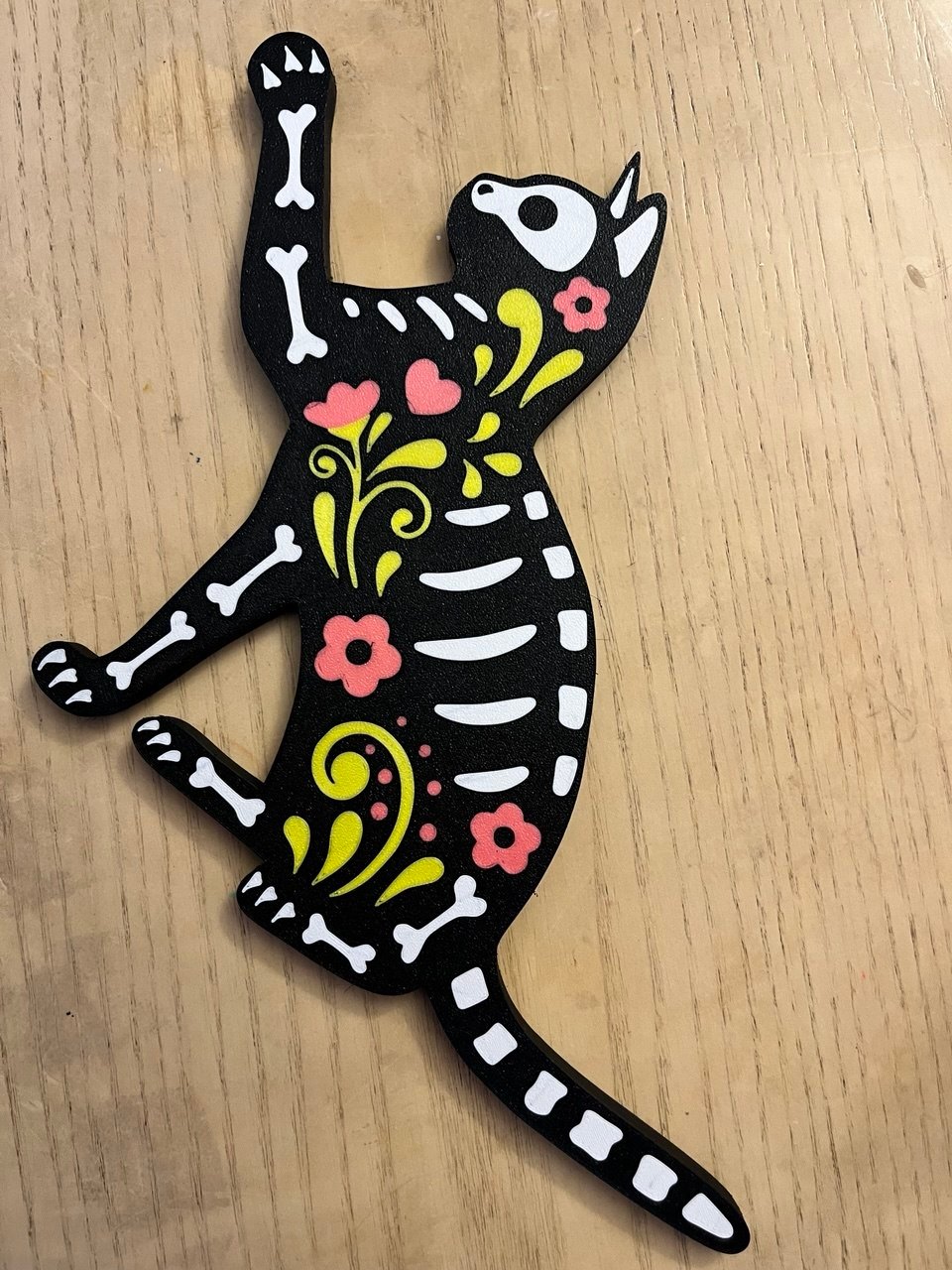 Gato negro decorativo con huesos blancos y flores rosas y amarillas.